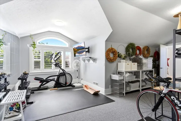 Vaulted ceiling featuring a large arched window with plantation shutters, light gray wall paneling, and a mounted flat-screen display