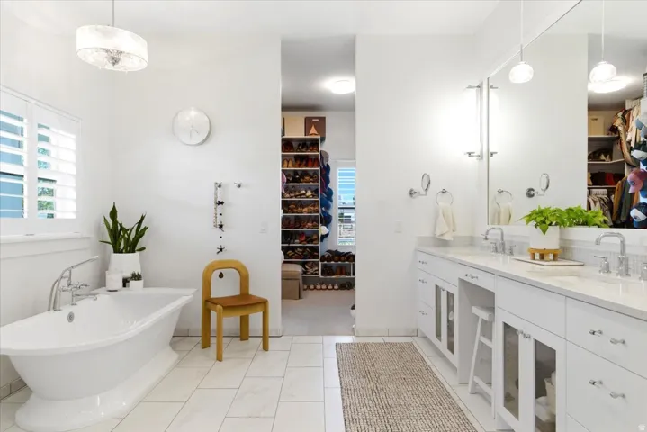 White bathroom featuring a freestanding soaking tub with chrome fixtures, a double vanity with stone countertops and undermount sinks, and a large mirror