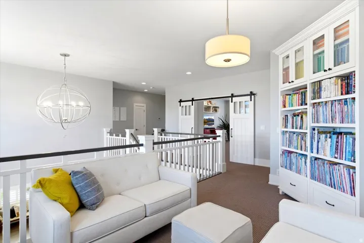 Open loft area featuring a contemporary drum pendant light, white baluster railings with black handrails, and built-in shelving with glass-front upper cabinets