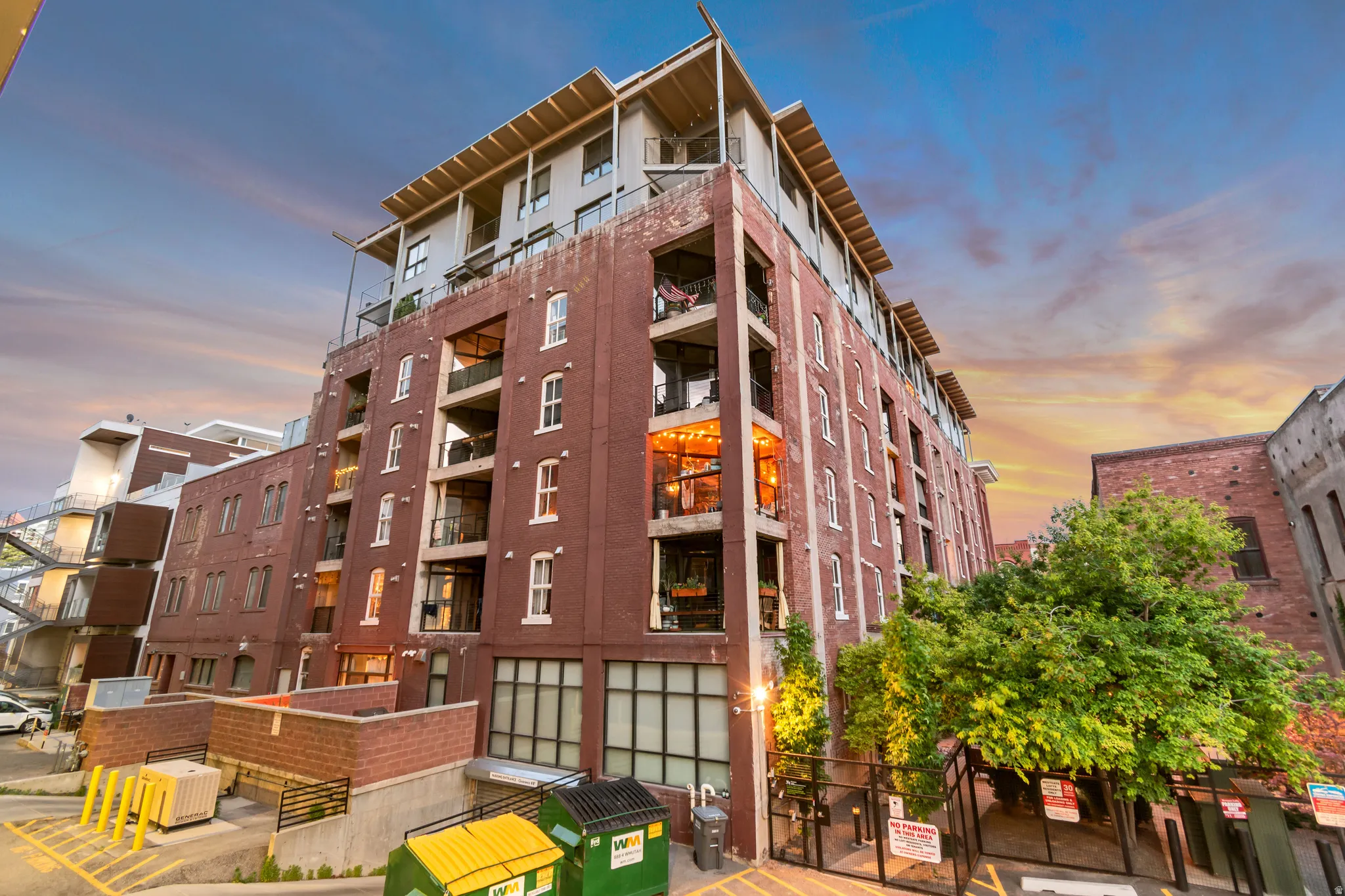 Multi-story brick building featuring balconies, large windows, and a modern top-floor addition with an overhang