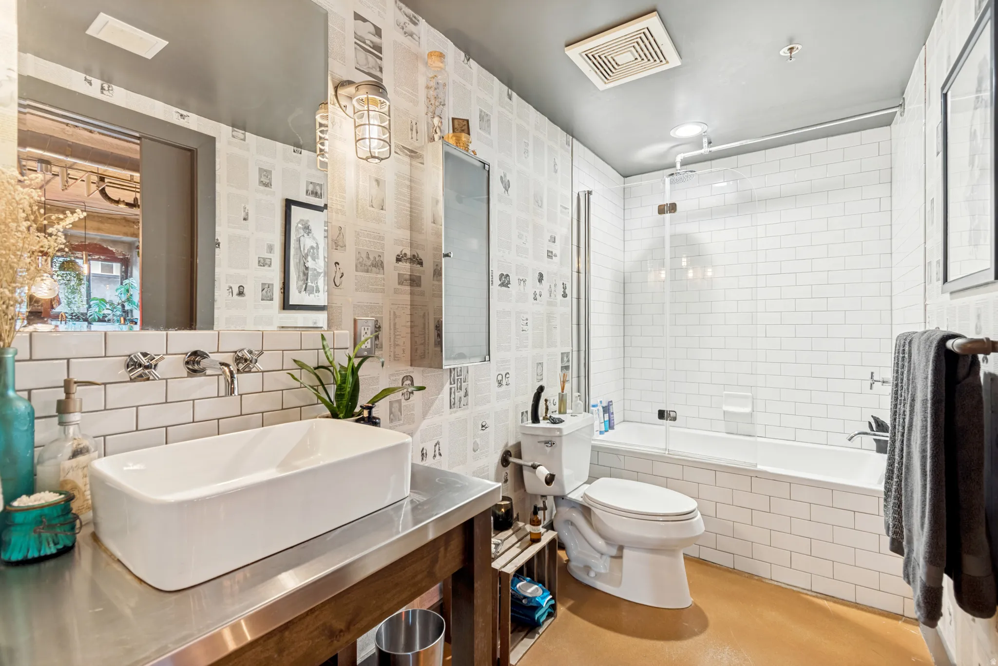 Bathroom featuring a rectangular vessel sink with wall-mounted faucets, a stainless steel countertop vanity, and a shower-over-tub combination with subway tile surround