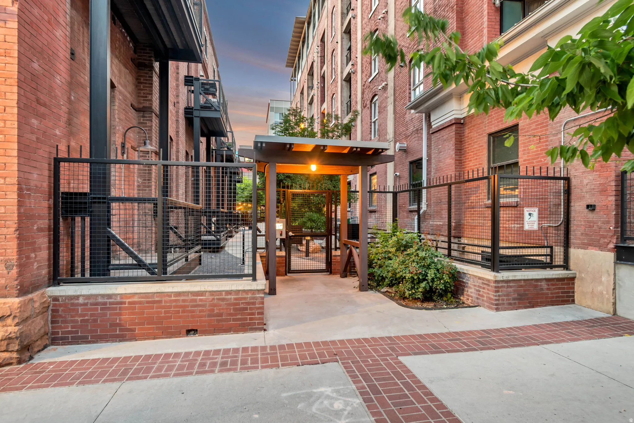 Outdoor common area featuring a covered walkway, integrated lighting, and brick pavers