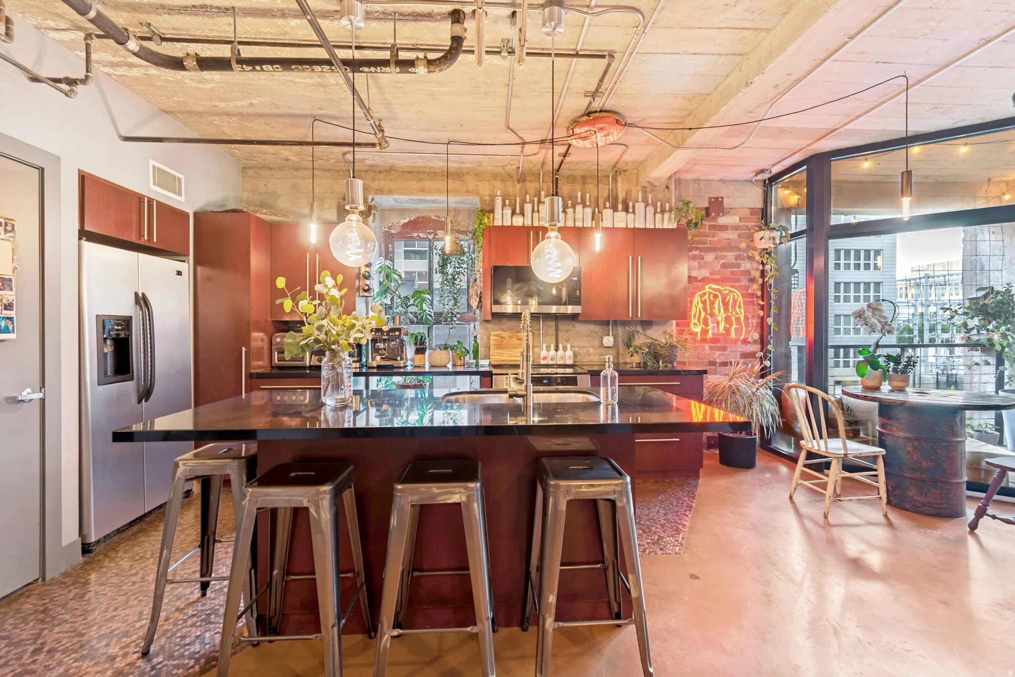 Open concept kitchen featuring an island with counter seating, stainless steel appliances, exposed brick accents, and concrete ceilings with visible ductwork