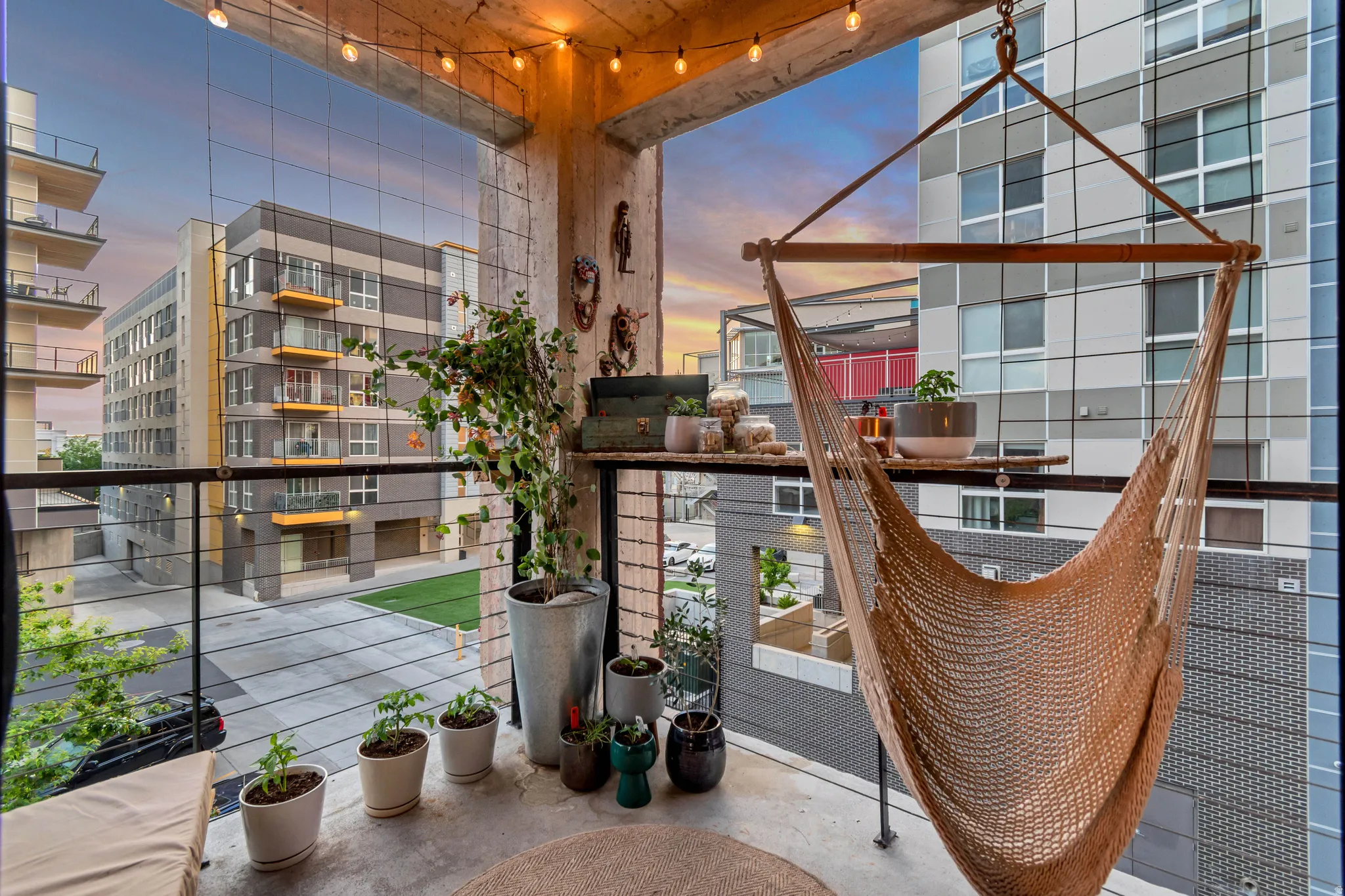 Concrete balcony with string lighting, wire railing, and a woven hammock chair