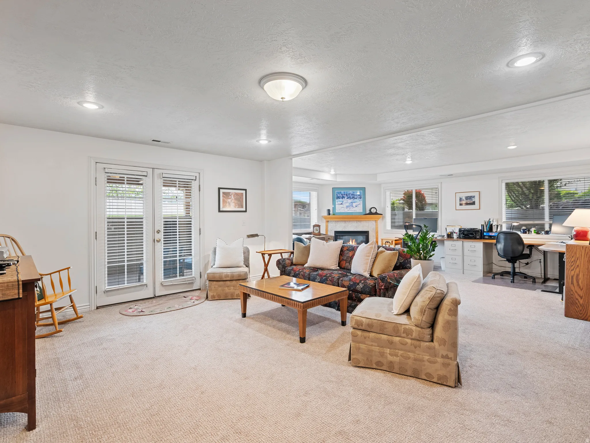 Spacious living area featuring light-colored carpeting, recessed lighting, and a prominent fireplace with a wood mantel