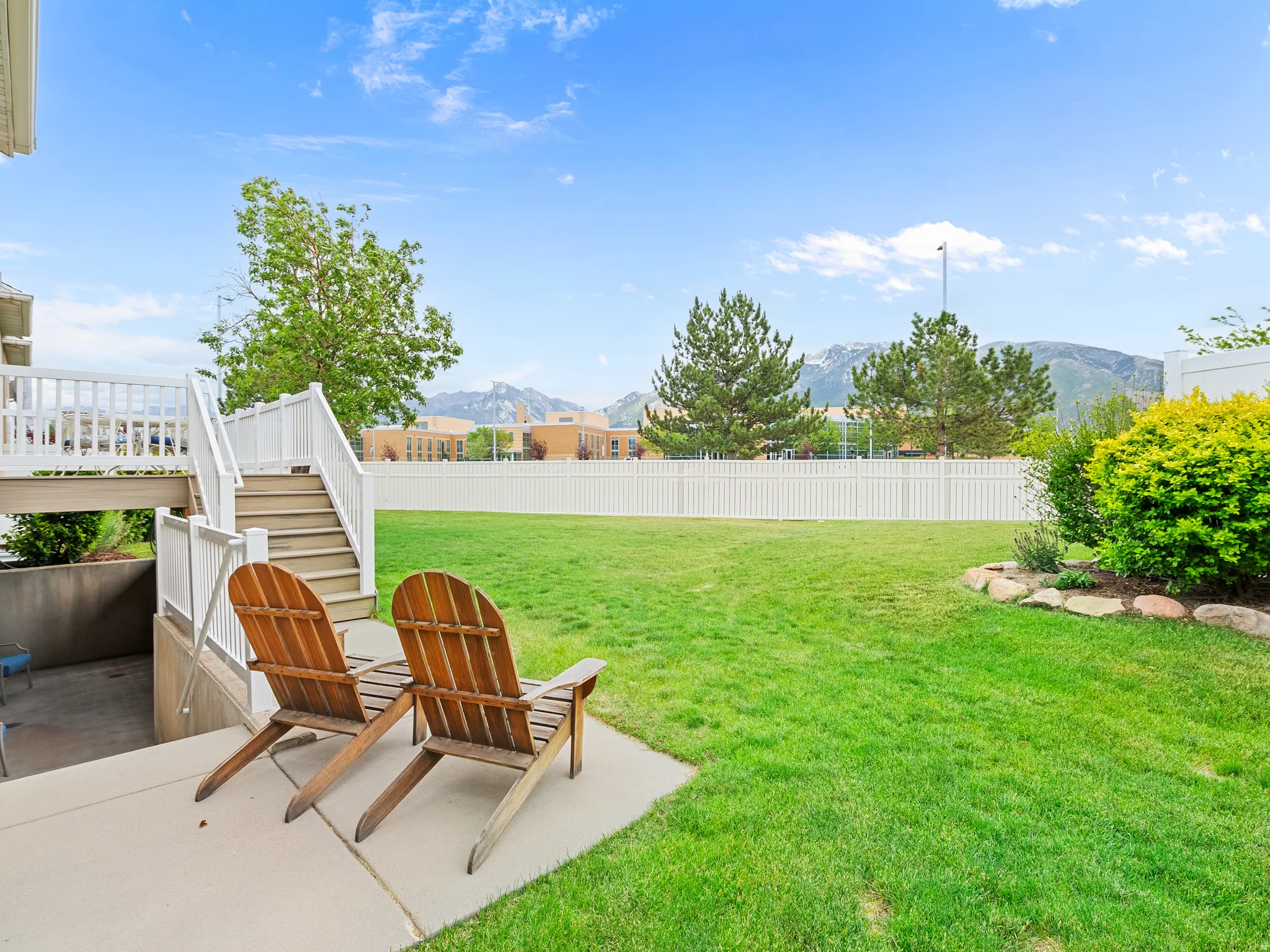 Expansive fenced backyard featuring a manicured lawn, established landscaping, and a concrete patio