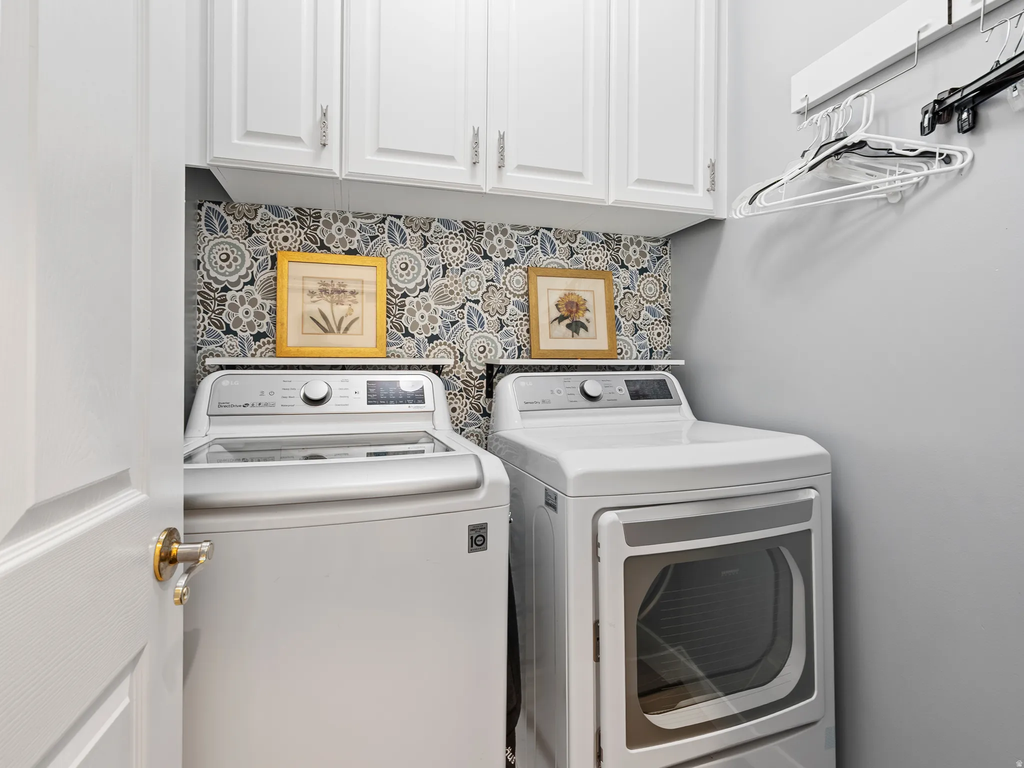 Dedicated laundry area featuring white shaker-style cabinetry, a floral-patterned accent wall, and a practical clothes hanging system