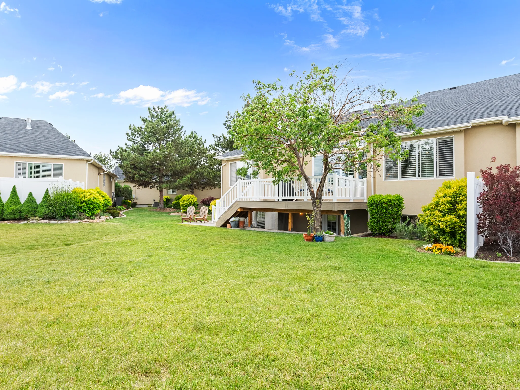 Spacious backyard featuring a multi-level deck with white railing, mature trees, and a manicured lawn