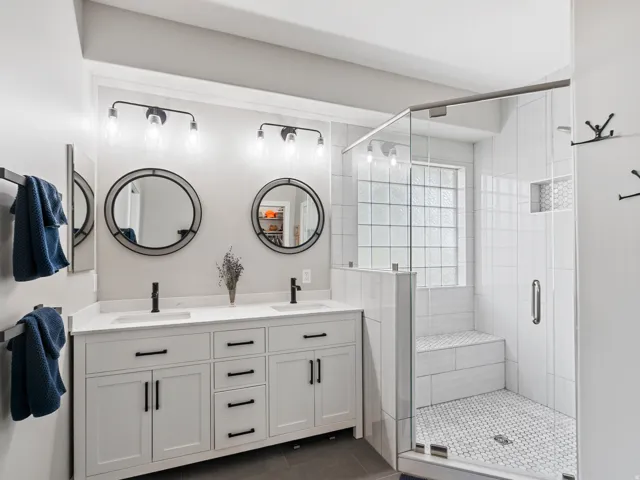 Bathroom featuring a double vanity with white cabinetry, black hardware, and two round mirrors