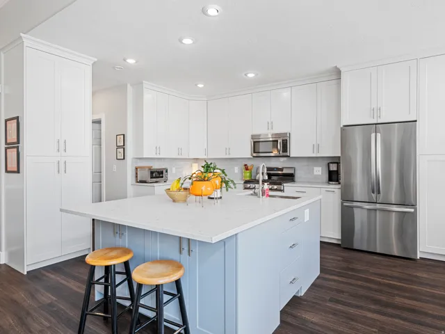 Contemporary kitchen featuring a light blue island with a bright countertop, stainless steel appliances, white cabinetry, recessed lighting, and wood-finish flooring