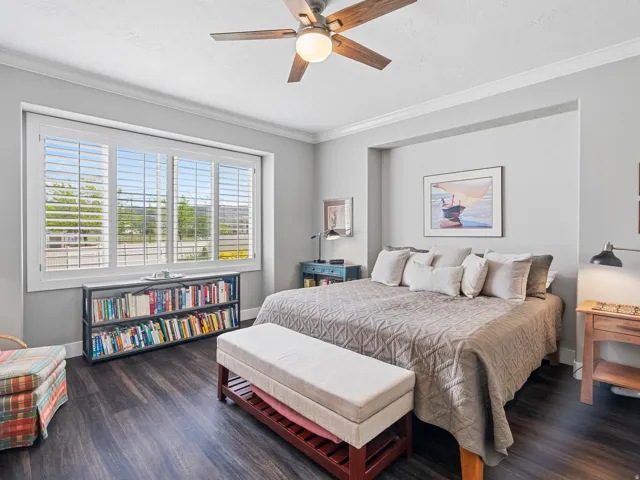 Spacious room featuring dark wood-finish flooring, a ceiling fan with light fixture, and crown molding