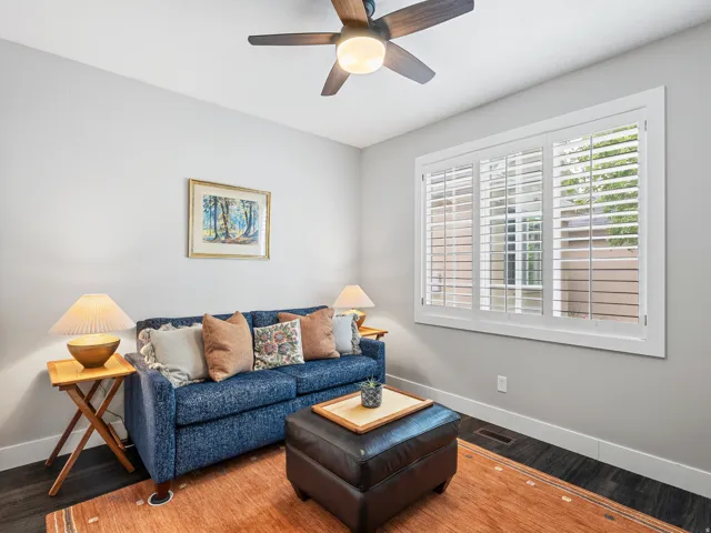 Inviting room featuring a window with white plantation shutters, rich wood-finish flooring, a ceiling fan with integrated lighting, and neutral wall tones