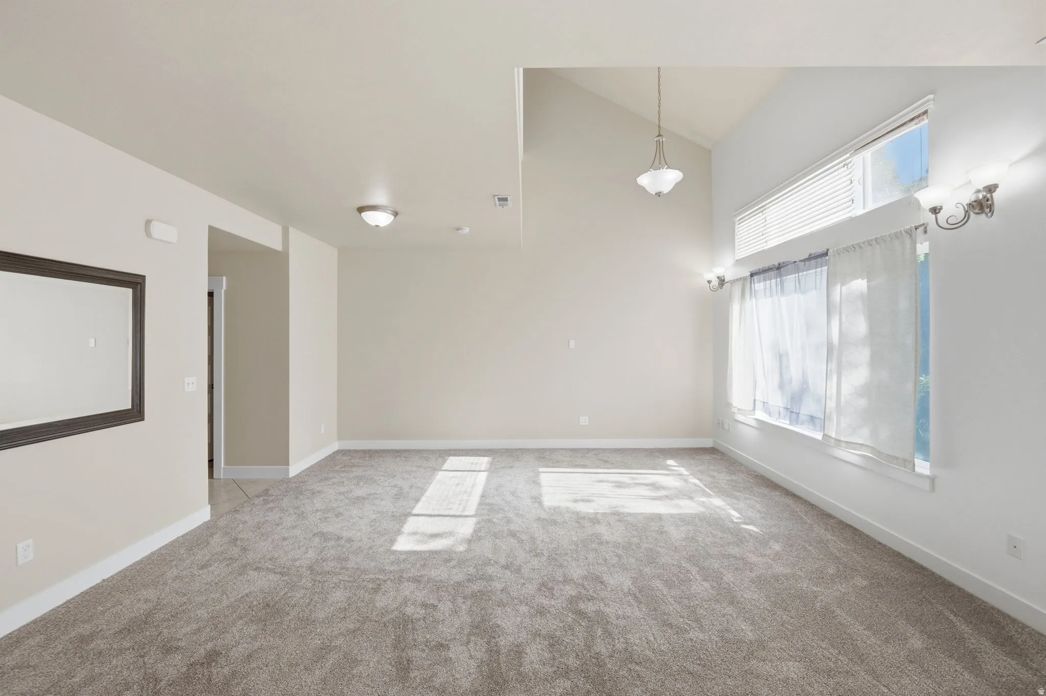 Spacious room featuring vaulted ceilings, neutral-toned carpeting, and a large window with an upper transom