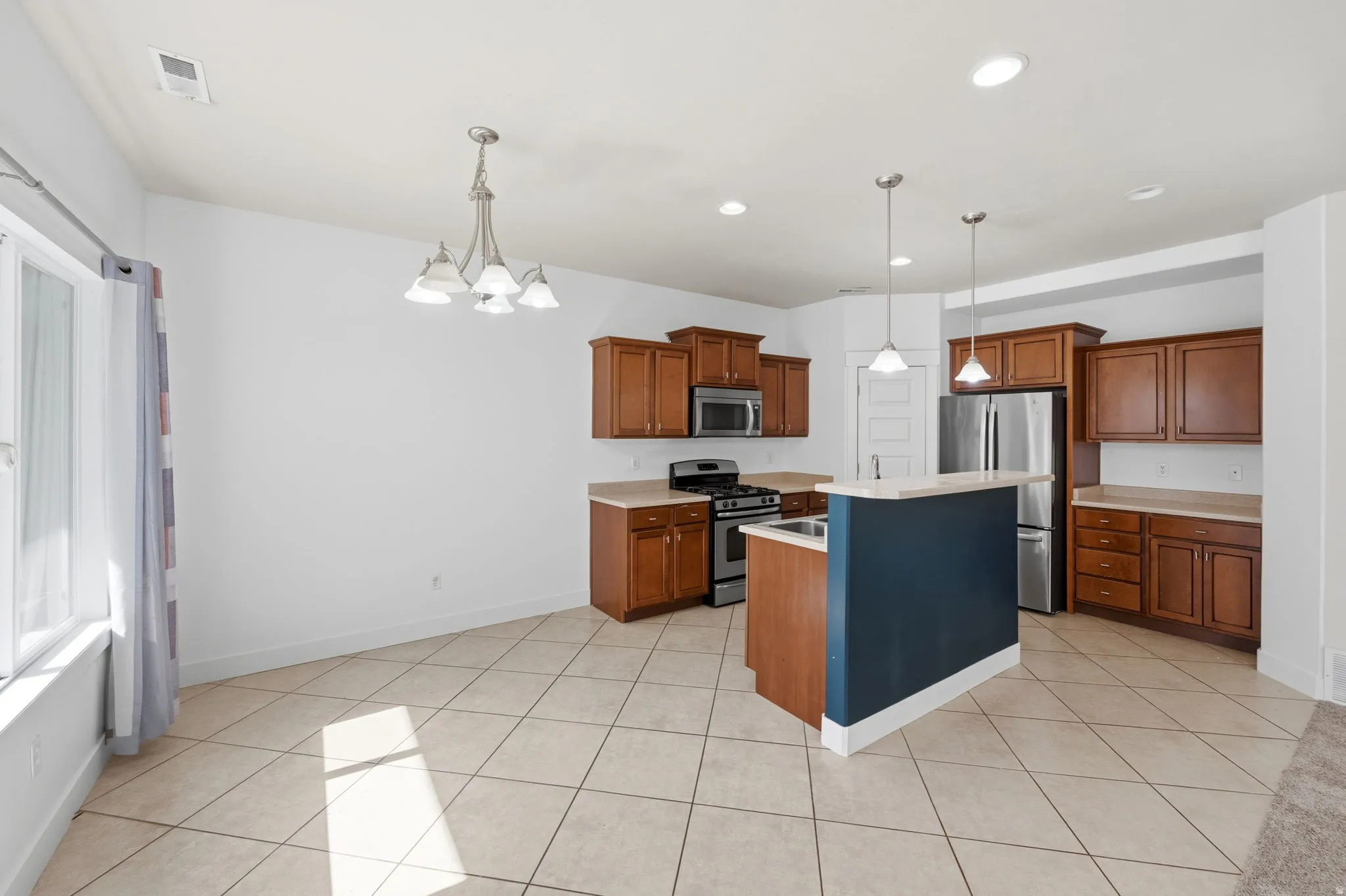 Open concept kitchen featuring warm wood cabinetry, stainless steel appliances, a center island with a breakfast bar, recessed lighting, and tile flooring