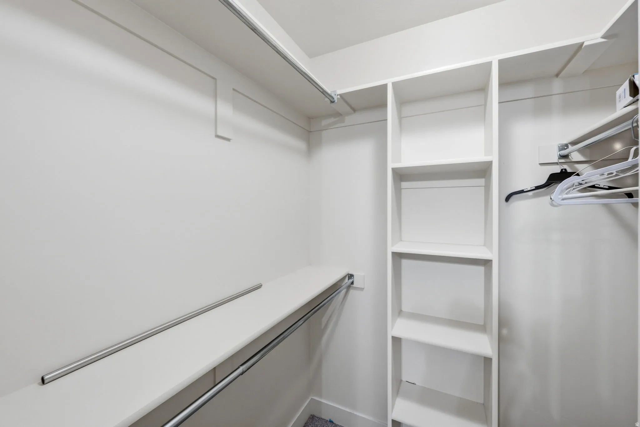 Walk-in closet featuring white built-in shelving, multiple hanging rods, and light-colored walls