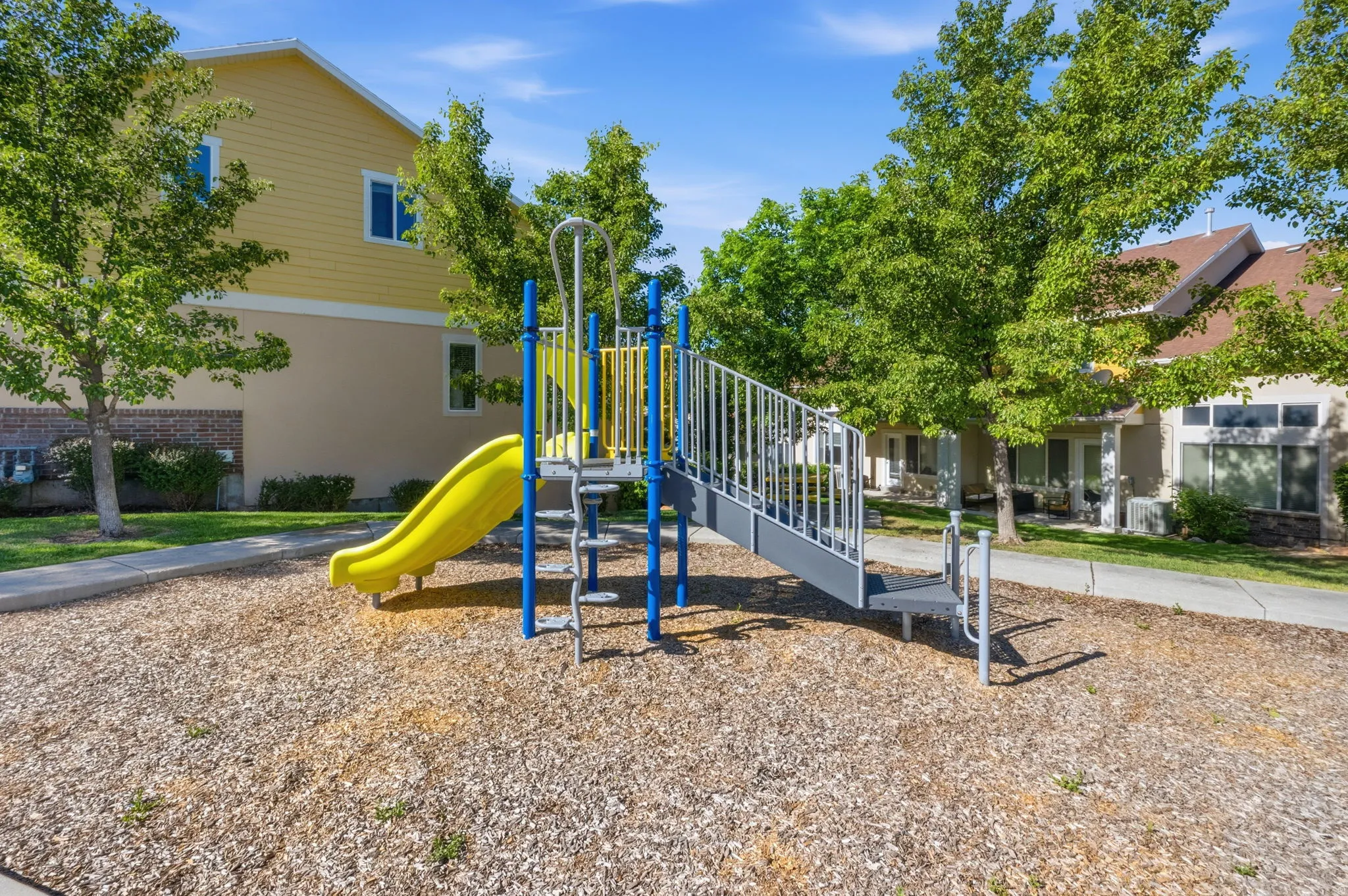 Outdoor recreational area featuring a colorful playset with a yellow slide, surrounded by wood chip surfacing
