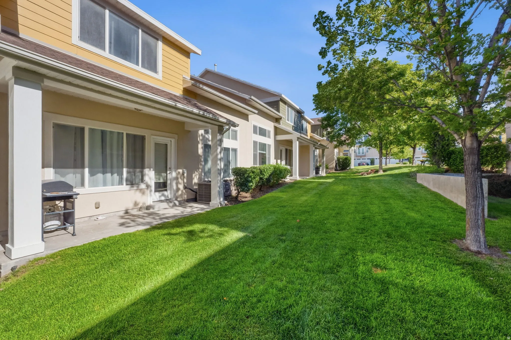 Expansive green space featuring mature trees and a concrete patio