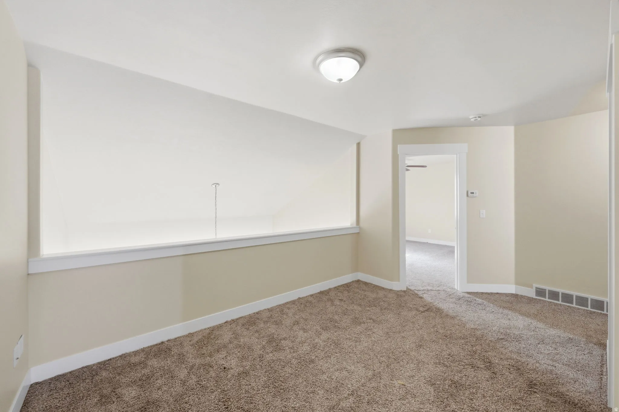 Carpeted interior space featuring a partial wall with white trim, an overhead flush-mount light fixture, and neutral-toned wall paint