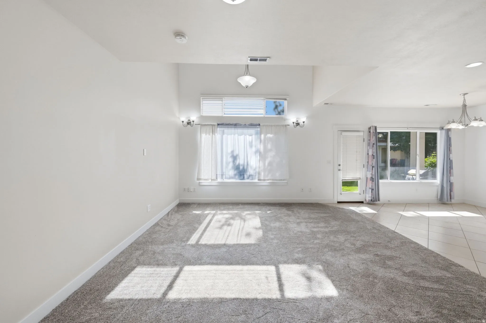 Spacious interior room featuring light gray carpet flooring transitioning to light-toned tile