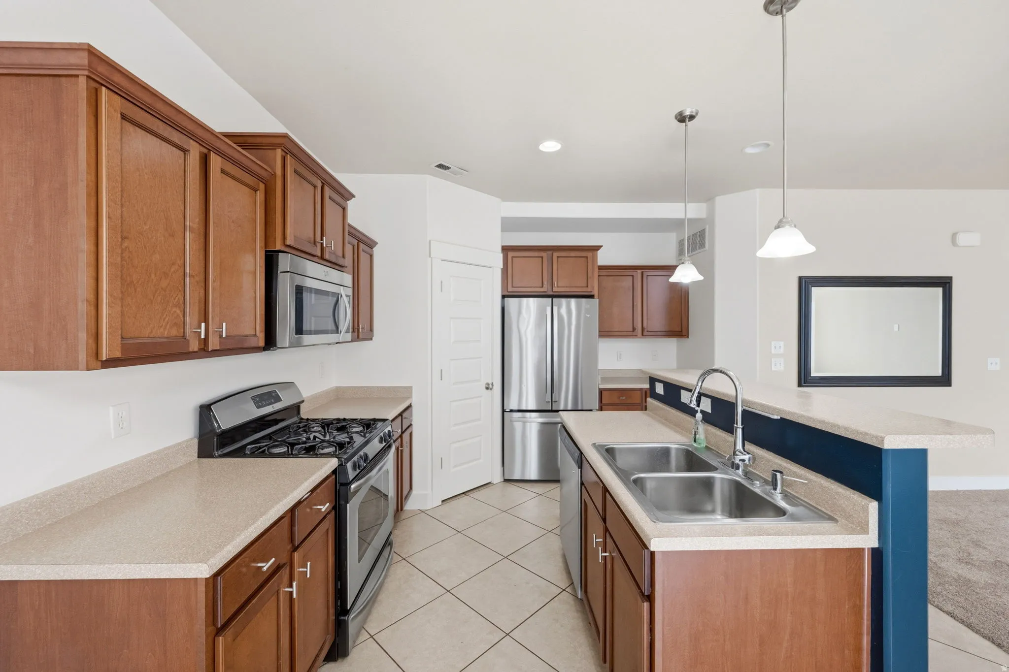 Open-concept kitchen featuring wood-finish cabinetry, light-toned countertops, and stainless steel appliances