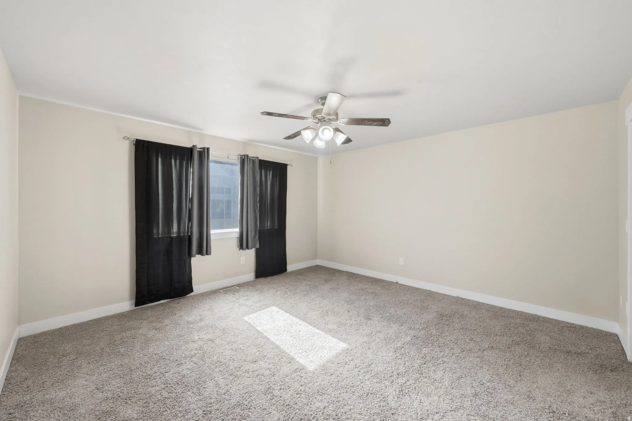 Spacious room featuring neutral carpet flooring, light-toned walls, and a ceiling fan with integrated lighting