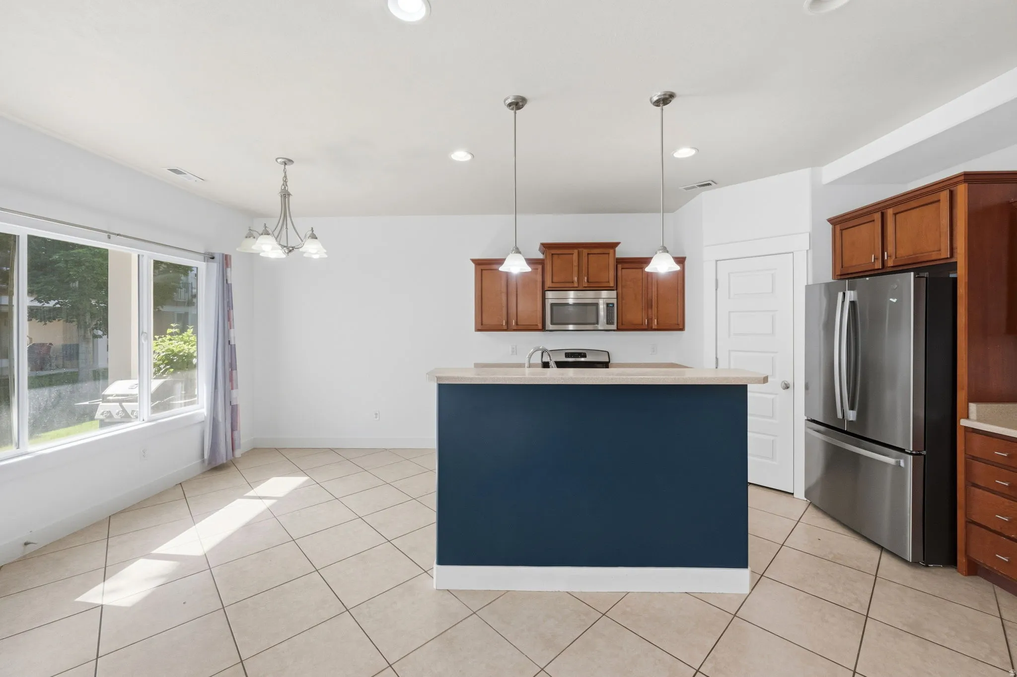 Kitchen and dining area featuring a central island with pendant lighting, stainless steel appliances, wood cabinetry, and tiled flooring