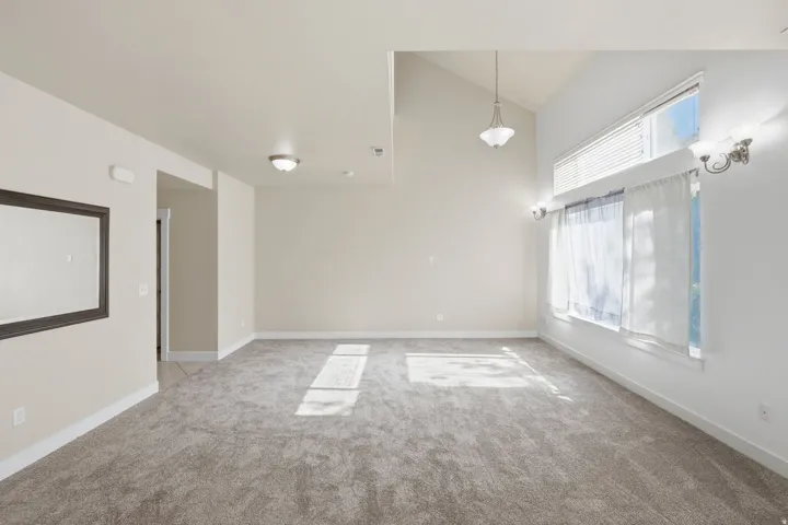 Spacious room featuring vaulted ceilings, neutral-toned carpeting, and a large window with an upper transom