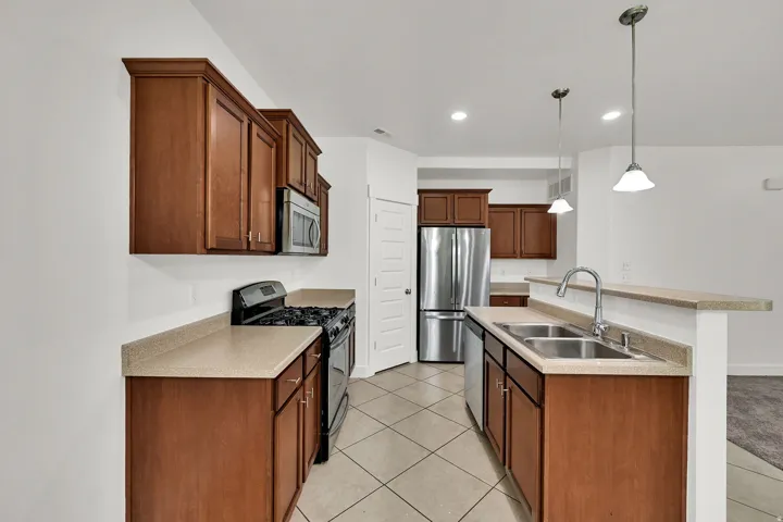 Kitchen featuring wood cabinetry, stainless steel appliances, a double basin sink with a high-arc faucet, and pendant lighting