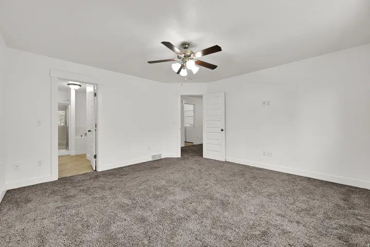 Spacious room featuring neutral carpeting, a ceiling fan with integrated lighting, and a white paneled door