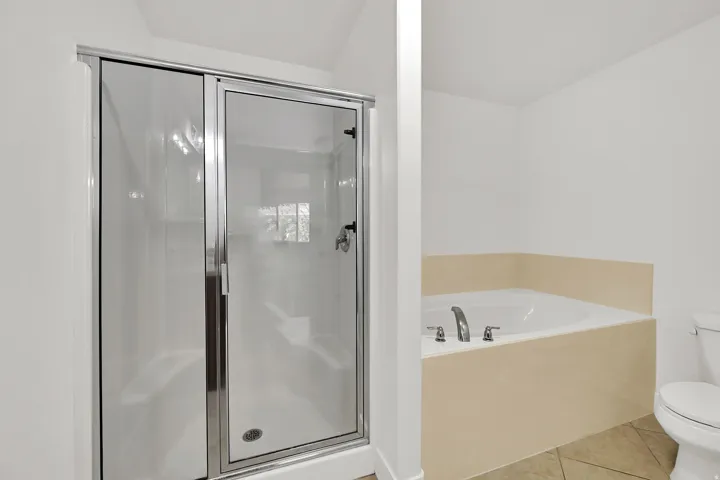 Enclosed shower with clear glass door, built-in corner bathtub with deck-mounted faucet, and light-toned floor tile