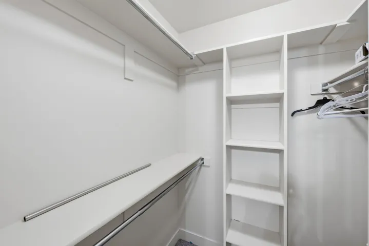 Walk-in closet featuring white built-in shelving, multiple hanging rods, and light-colored walls