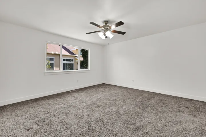 Spacious room featuring neutral carpeting, white walls, and a ceiling fan with integrated lighting