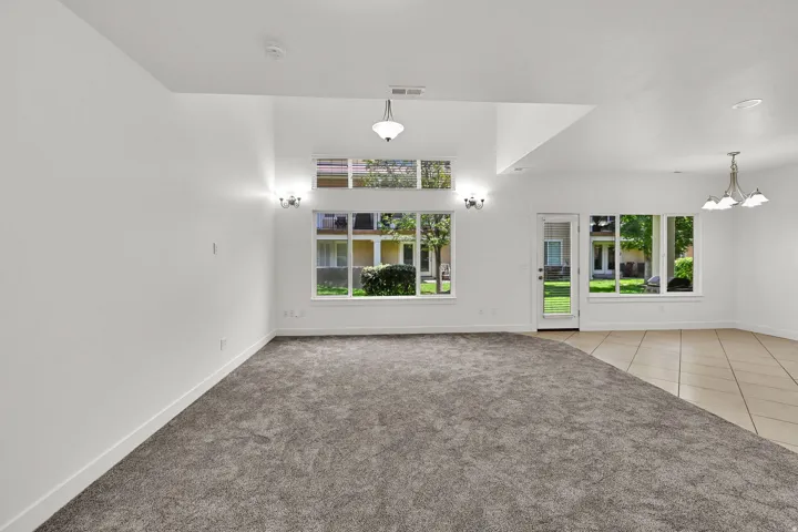 Vaulted ceiling with integrated lighting, expansive windows, glass-paneled door, and a tiled flooring section