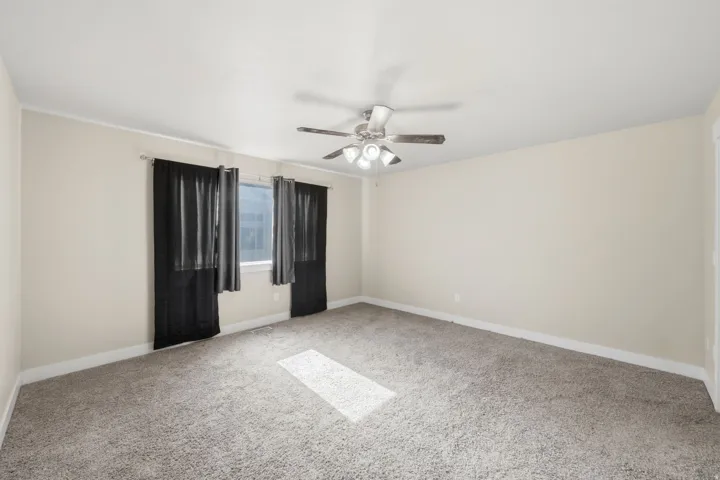 Spacious room featuring neutral carpet flooring, light-toned walls, and a ceiling fan with integrated lighting