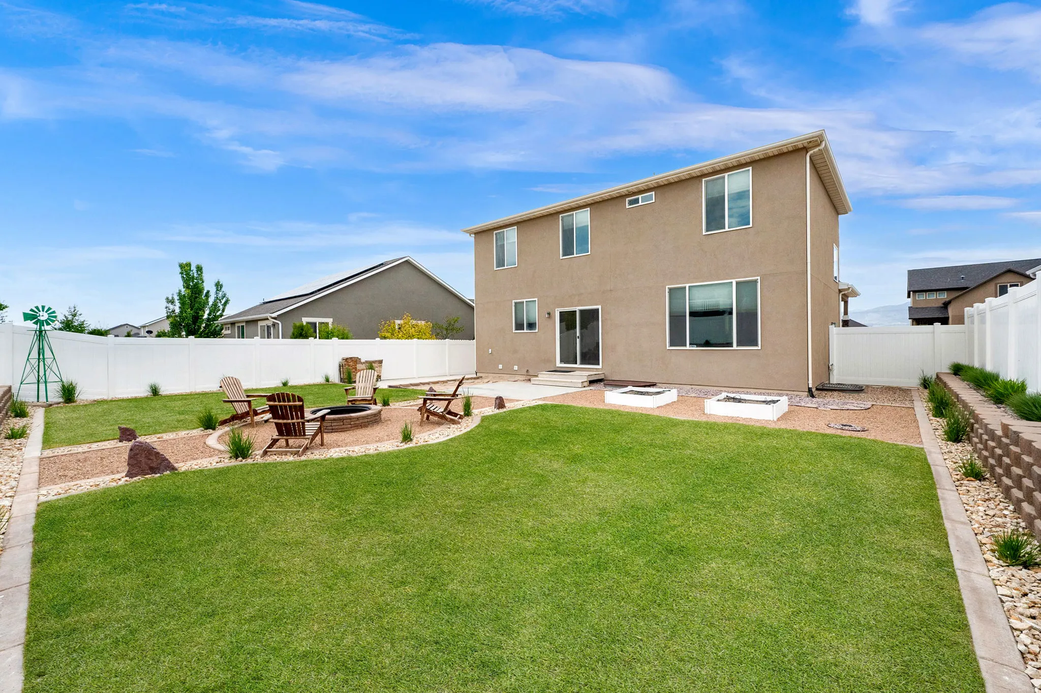 Expansive backyard featuring a lush green lawn, a brick-lined fire pit area with gravel pathways, and a white vinyl privacy fence