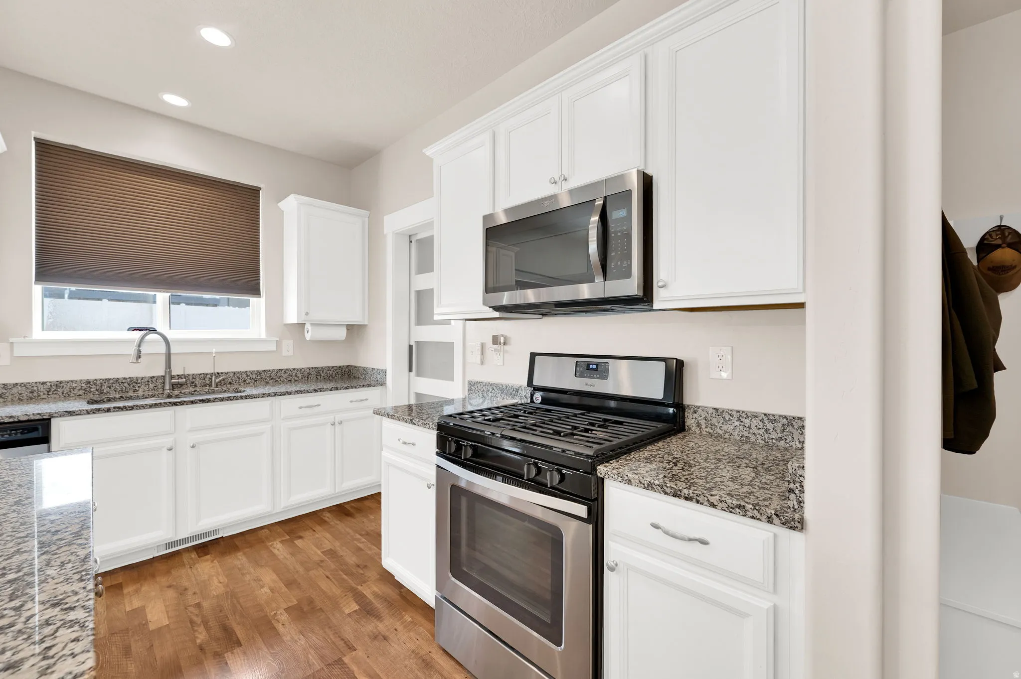 Kitchen featuring white cabinetry, stainless steel appliances, speckled stone countertops, a gas range, and wood-finish flooring