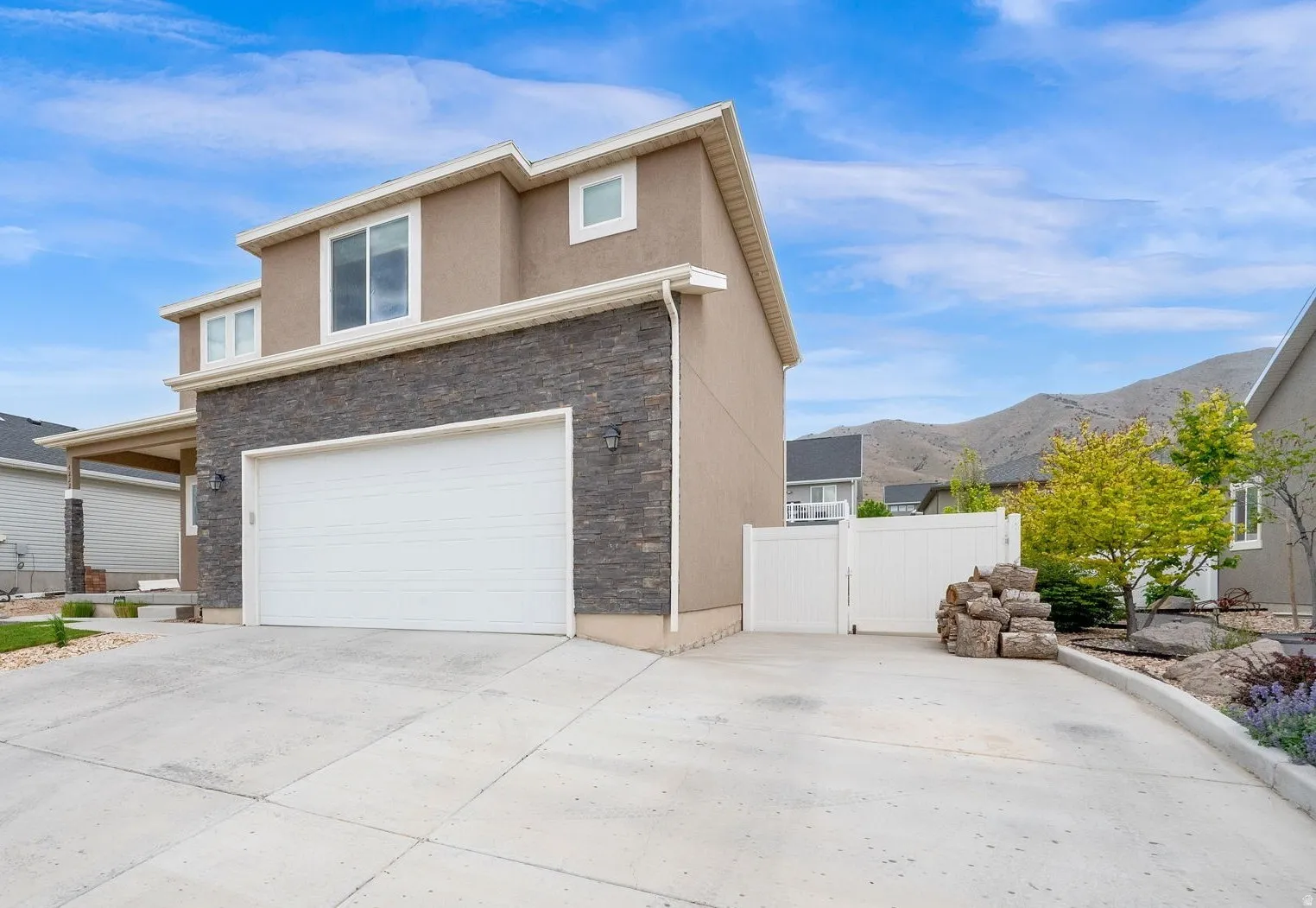 Stucco exterior featuring stacked stone accents, an attached garage, a side yard with a white vinyl fence, and a mountain backdrop