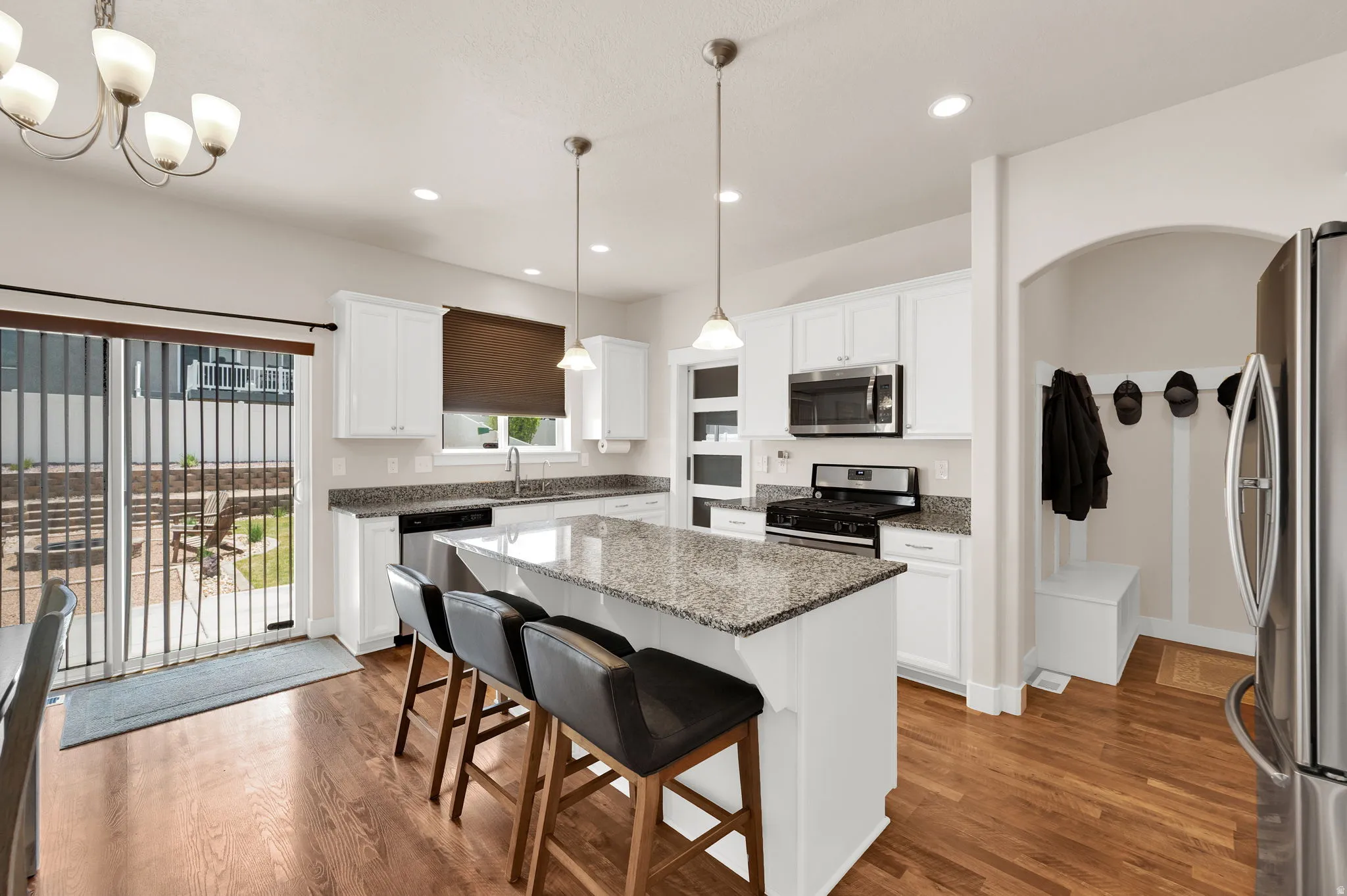 Open-concept kitchen featuring white cabinetry, granite countertops, stainless steel appliances, and wood-finish flooring
