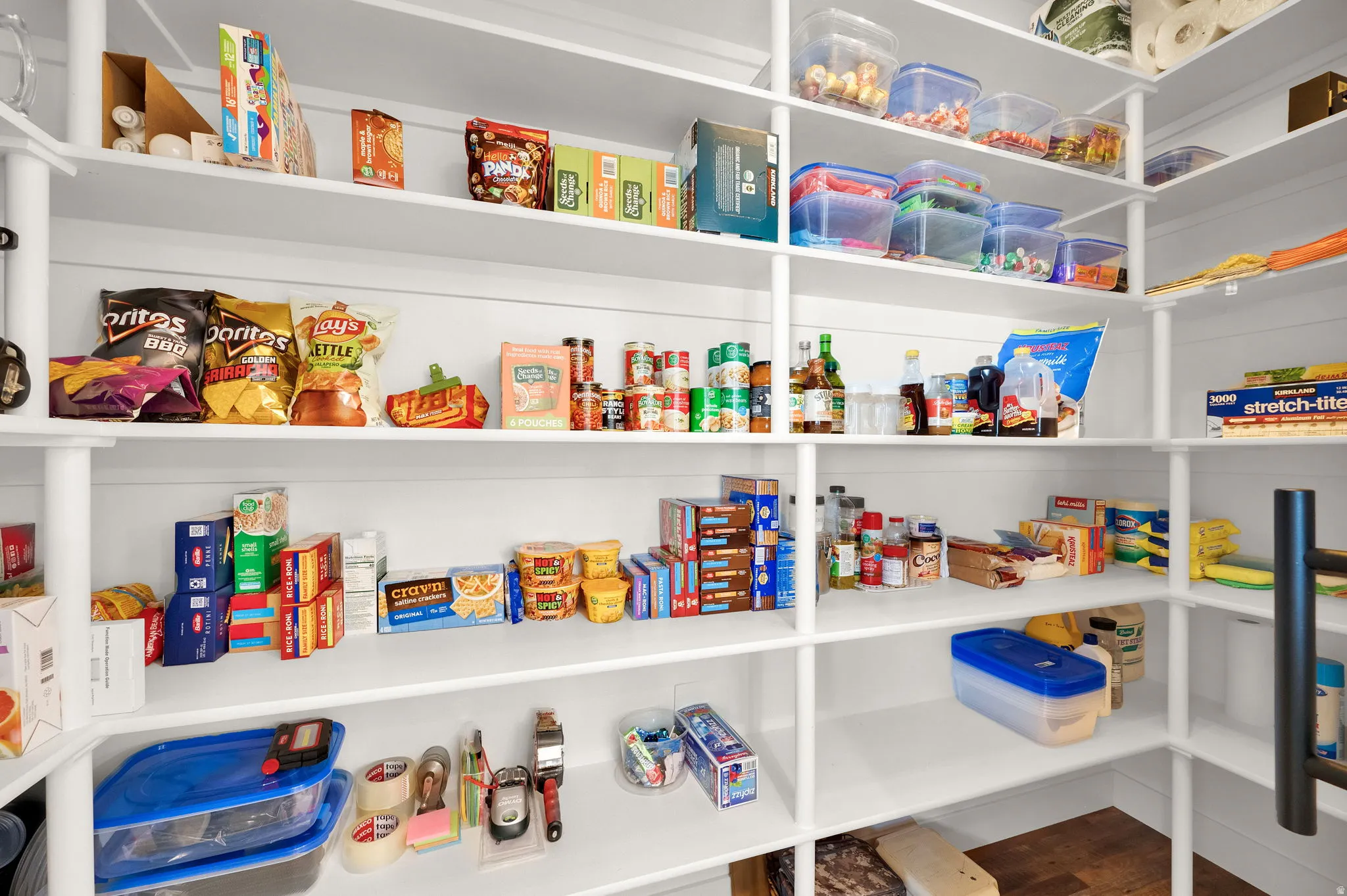 Expansive pantry featuring white shelving with vertical supports, corner shelving, and wood-finish flooring