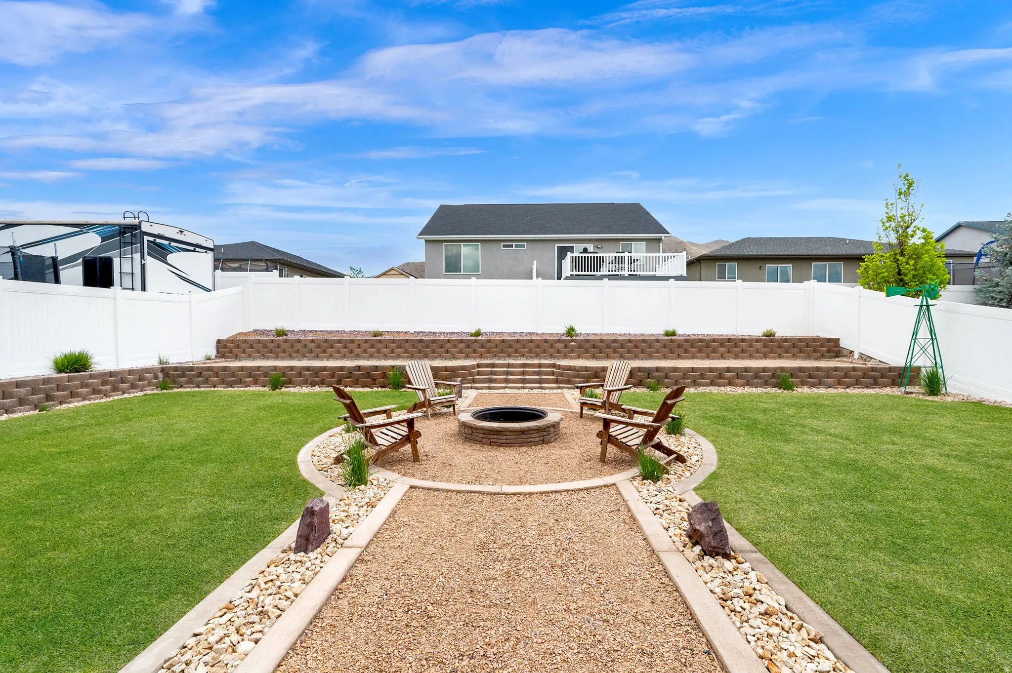 Expansive backyard featuring a central fire pit area with gravel hardscaping, surrounded by a lush lawn