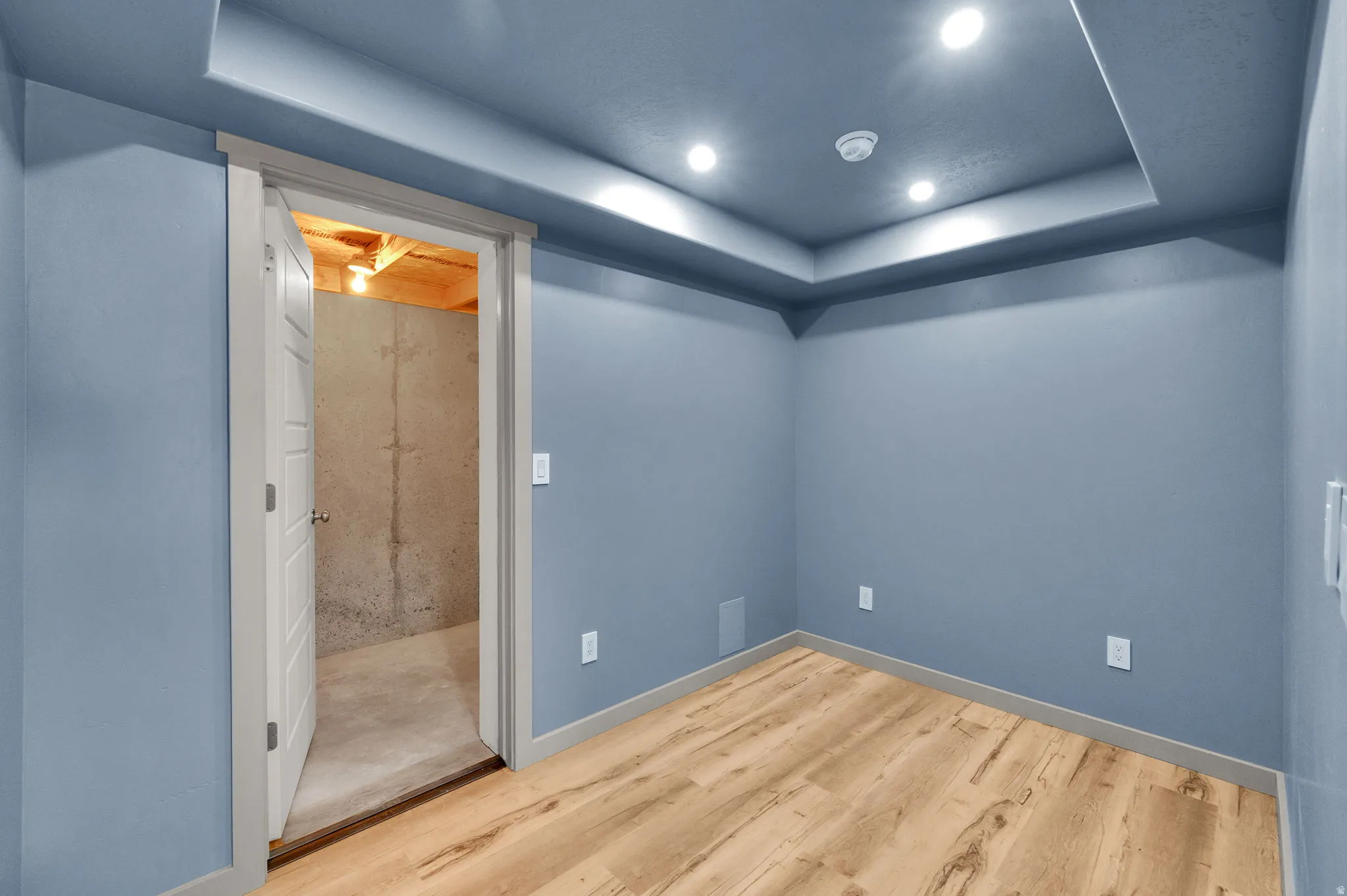 Room featuring light wood-finish flooring, blue-painted walls, and a recessed ceiling with integrated lighting