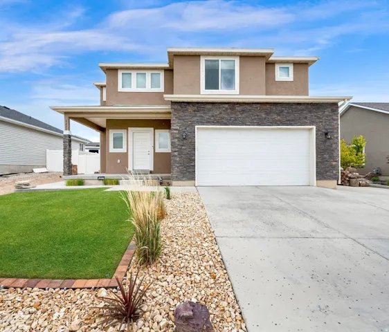 Contemporary two-story residence featuring a stone and stucco exterior, an attached two-car garage, a covered entry porch with stone-clad columns, a concrete driveway, and a front yard with a lawn and decorative rock landscaping