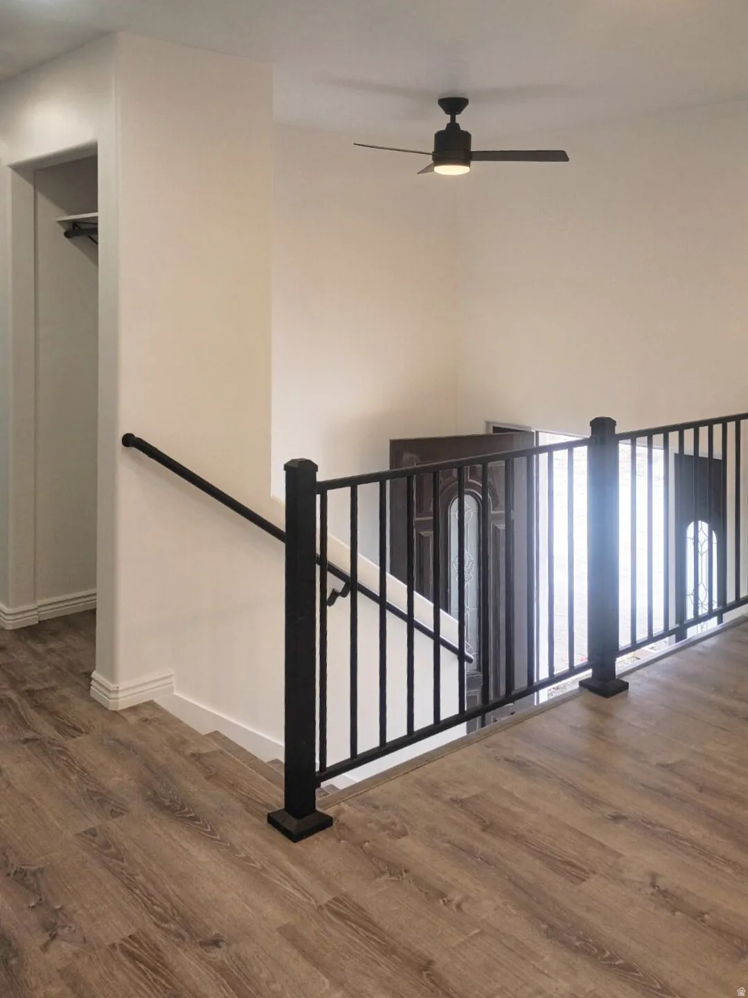 Upper-level landing featuring wood-finish flooring, a black metal railing, and a contemporary ceiling fan with integrated lighting