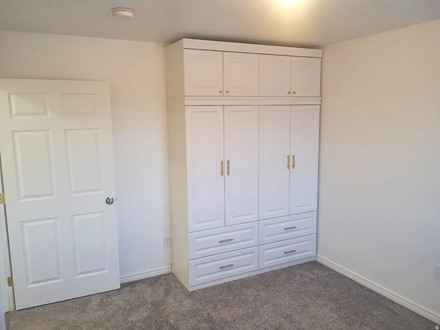 Built-in white cabinetry with gold-finish hardware and integrated drawers, light gray carpeting, and white baseboards