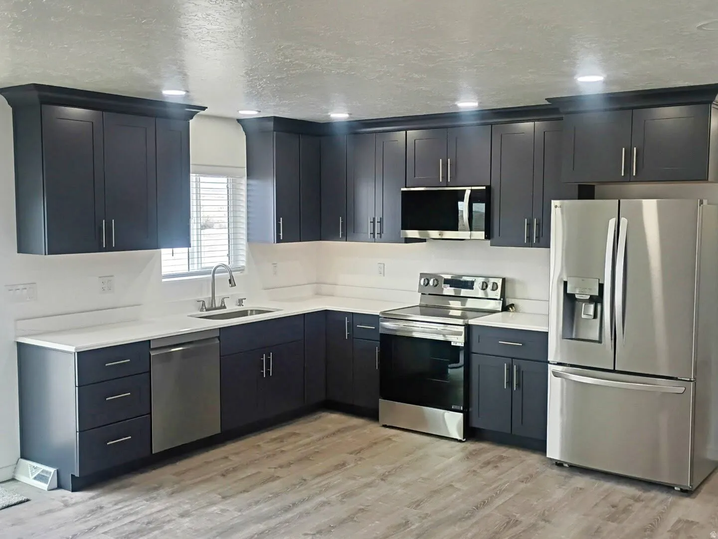 Contemporary kitchen featuring dark cabinetry, white countertops, recessed lighting, stainless steel appliances, and wood-finish flooring