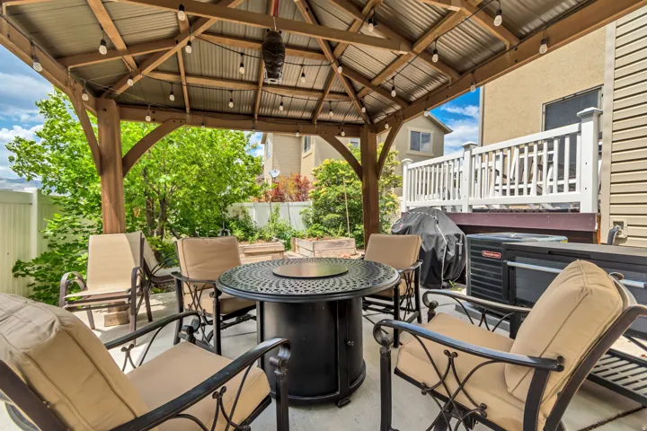 Covered patio featuring a wood-framed gazebo with a corrugated metal roof, string lighting, and a built-in fire pit