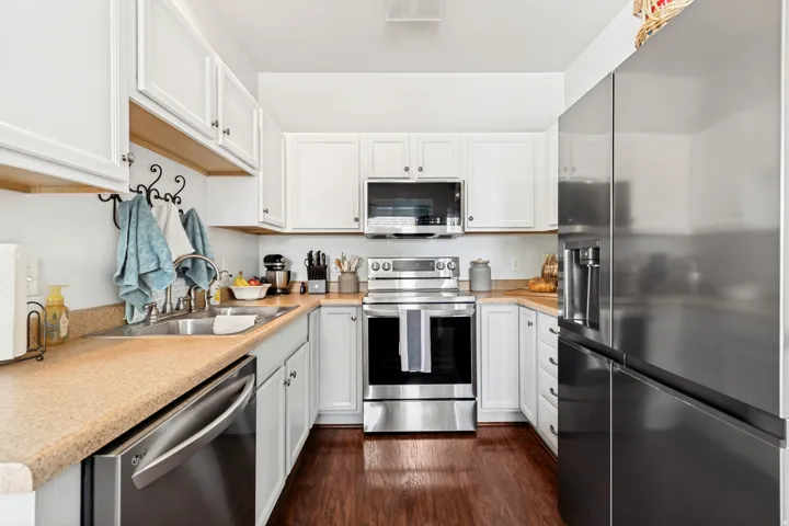 U-shaped kitchen featuring white cabinetry, stainless steel appliances, wood-finish flooring, a stainless steel sink, and light-toned countertops