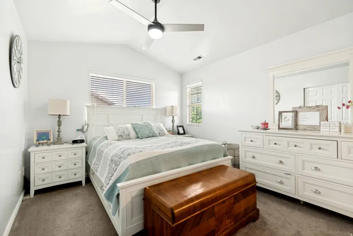 Vaulted ceiling bedroom featuring carpet flooring, natural light through window blinds, and a ceiling fan