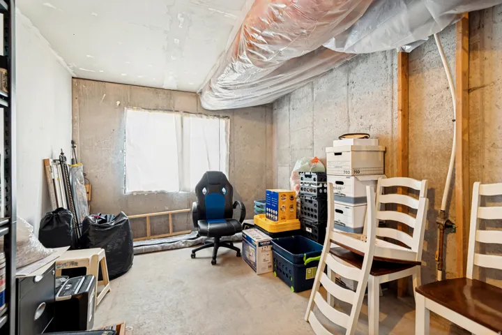 Unfinished basement area featuring concrete walls, a single window opening, visible exposed ductwork, and exposed wooden framing