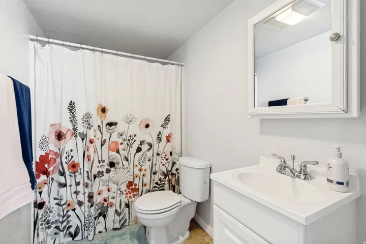 Bathroom featuring a white toilet, a vanity with an integrated sink, a chrome two-handle faucet, and a wall-mounted medicine cabinet with a mirror